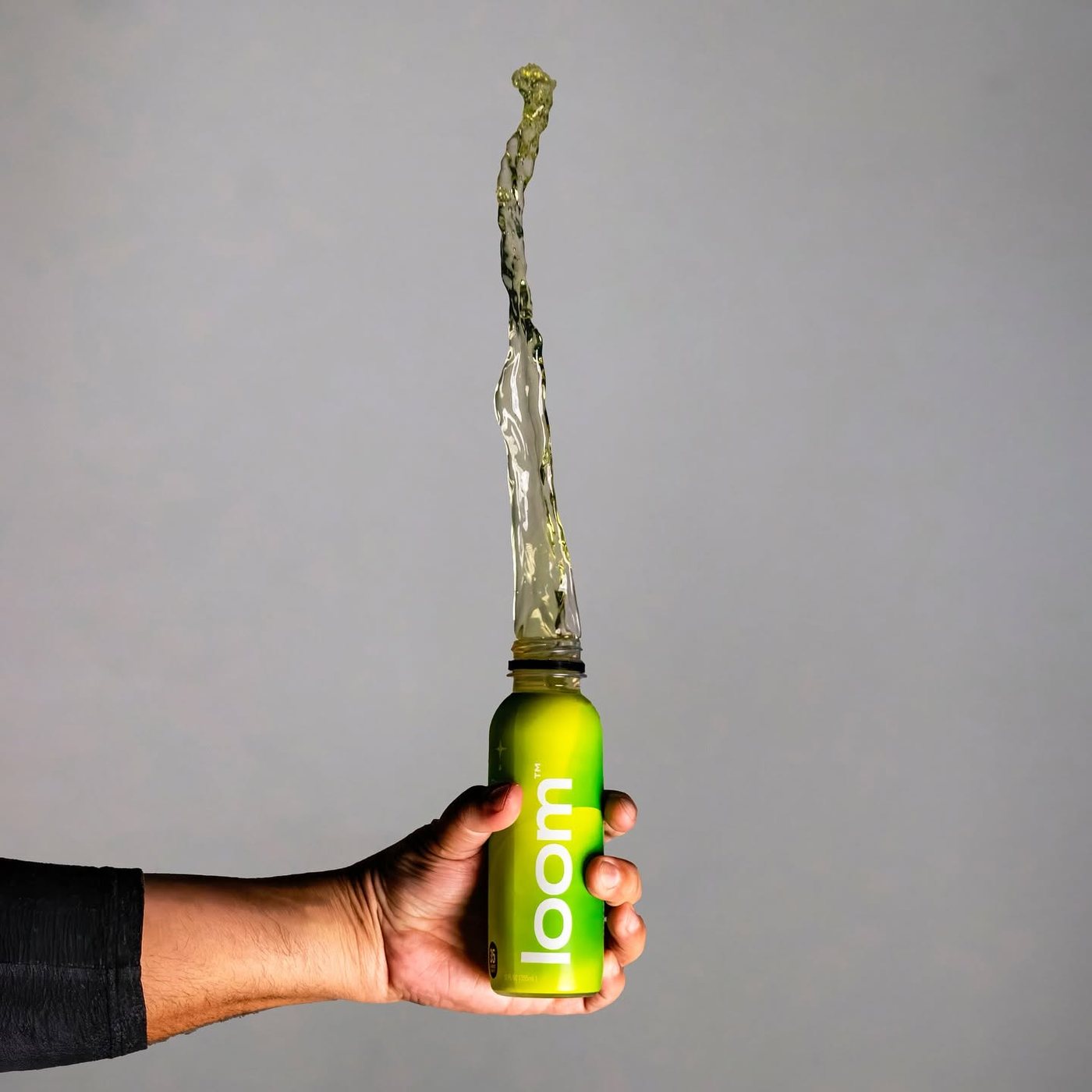 Hand holding a loom bottle with juice arcing out of the top, shot for loom