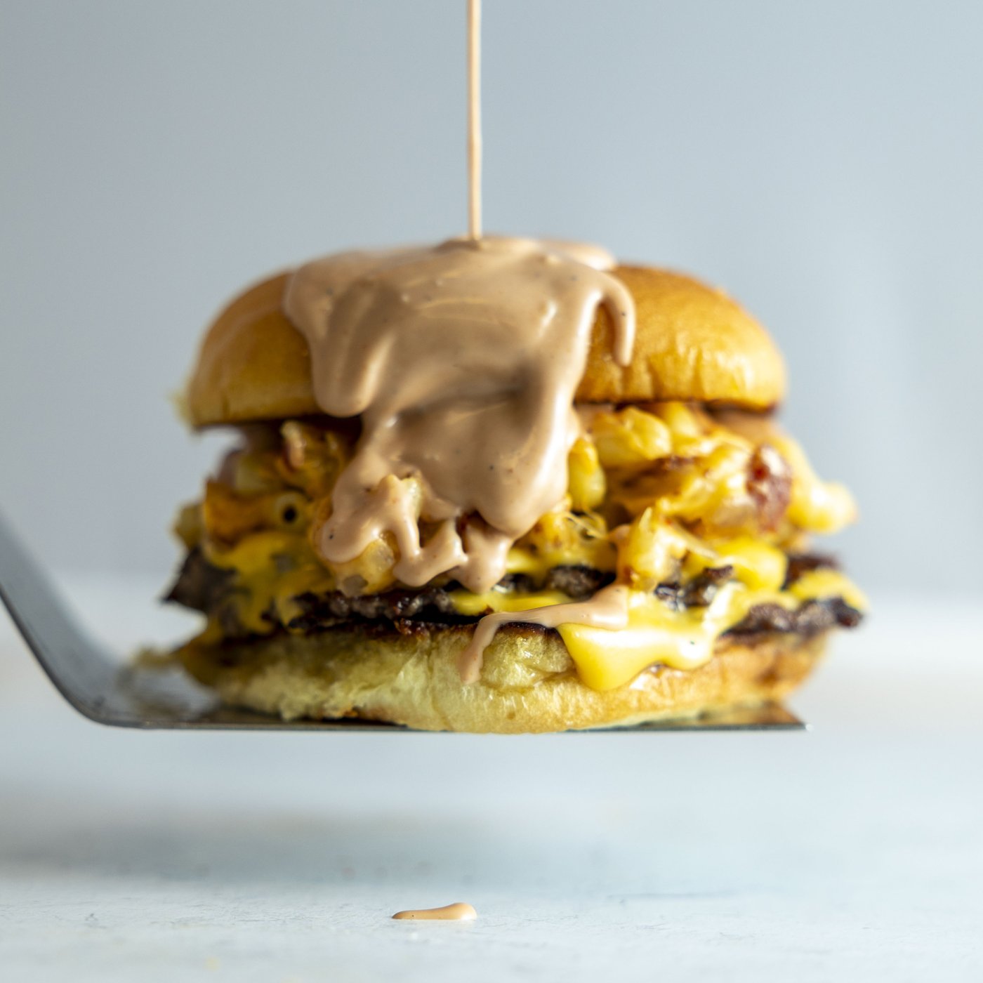 Double smash burger with mac and cheese and house sauce on a spatula, shot at The Quarry Grill