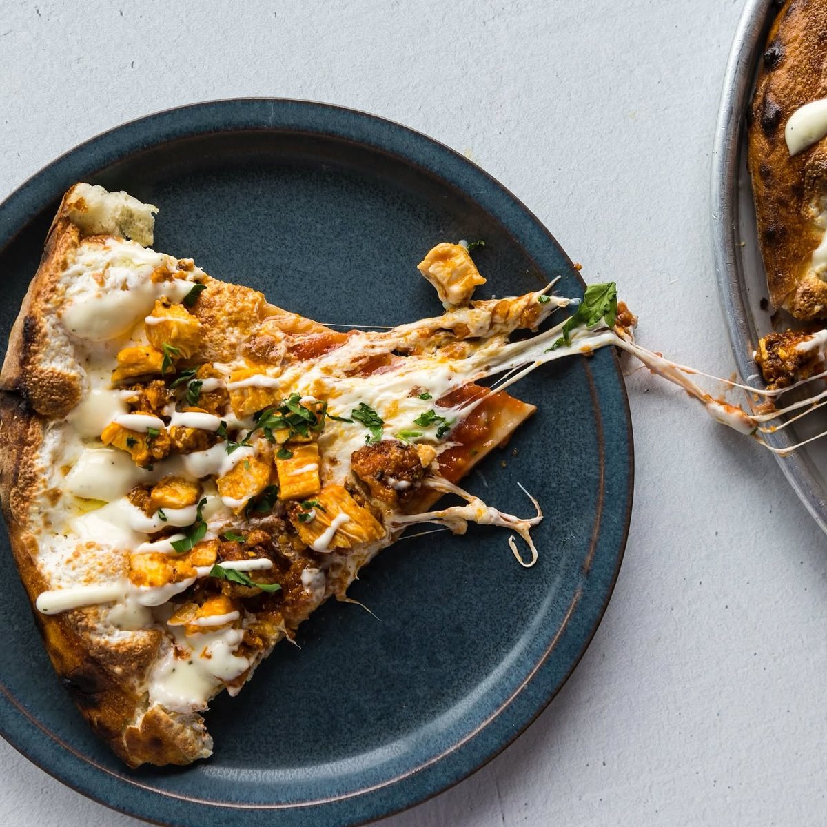 Buffalo chicken slice lifted from the pan with the cheese still pulling, shot by Wildcat