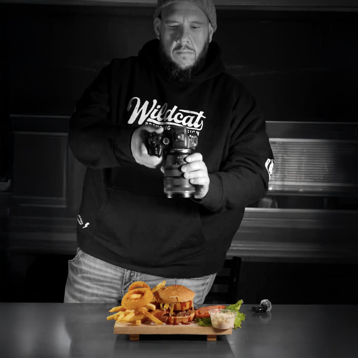 Wildcat photographer in a Wildcat hoodie shooting a burger platter, black and white with the food in color